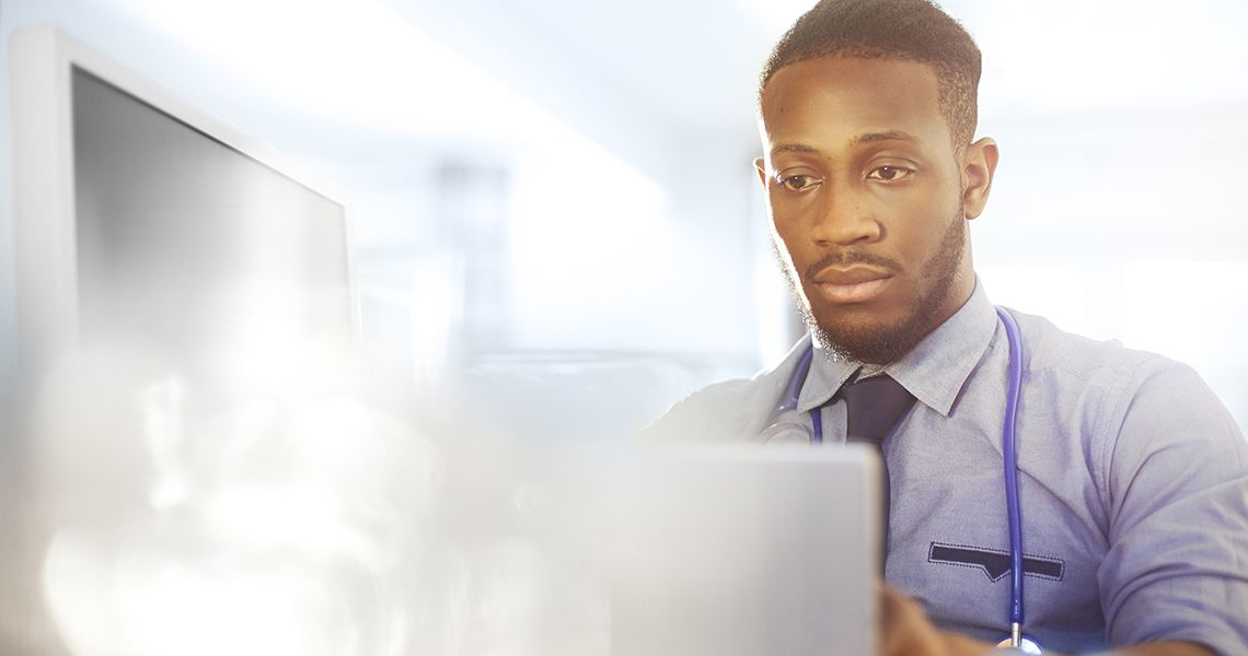 doctor with a stethoscope around his neck looking at a laptop