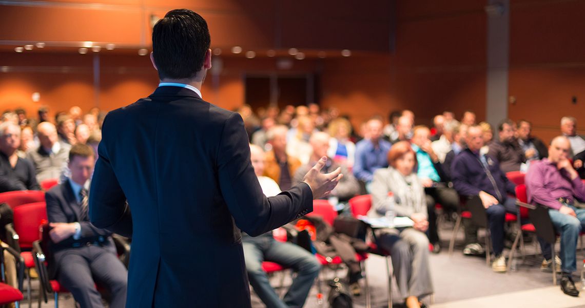 Person standing in front of an audience of people speaking